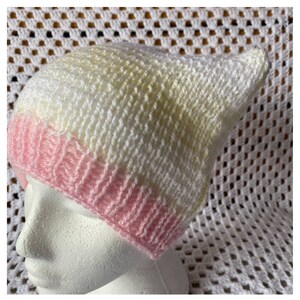 May include: A knitted hat with a pink, white and yellow ombre design. The hat is made of soft yarn and has a slouchy fit.