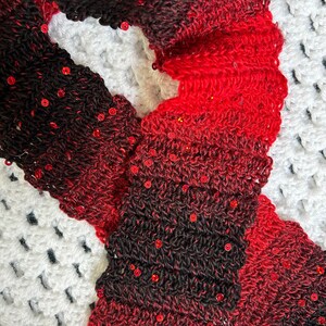 May include: A red and black crocheted scarf with sequins. The scarf is made with a gradient of red and black yarn and has a textured look.