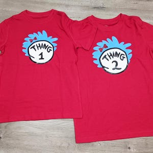 May include: Two red t-shirts with Thing 1 and Thing 2 designs from the book "The Cat in the Hat".