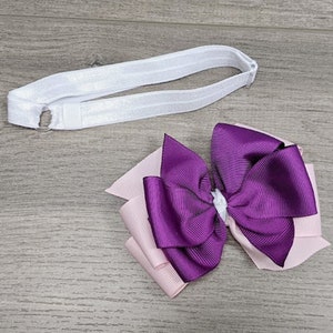 Op de afbeelding: Een paarse en roze strik met een wit elastisch hoofdband. De strik is gemaakt van twee lagen lint, waarbij de bovenste laag paars is en de onderste laag roze.