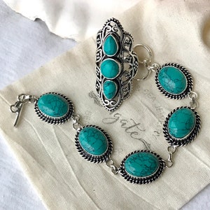 K&ouml;nnte beinhalten: Ein silbernes Armband mit t&uuml;rkisfarbenen Steinen und ein passender silberner Ring mit t&uuml;rkisfarbenen Steinen. Das Armband hat einen Verschluss und der Ring hat ein offenes Design.