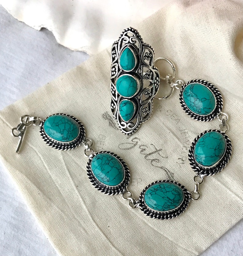 K&ouml;nnte beinhalten: Ein silbernes Armband mit t&uuml;rkisfarbenen Steinen und ein passender silberner Ring mit t&uuml;rkisfarbenen Steinen. Das Armband hat einen Verschluss und der Ring hat ein offenes Design.