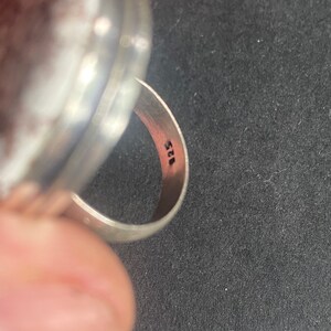 K&ouml;nnte beinhalten: Ein silberner Ring mit einer runden, glatten Oberseite und einem Band, das mit der Nummer "925" gekennzeichnet ist.