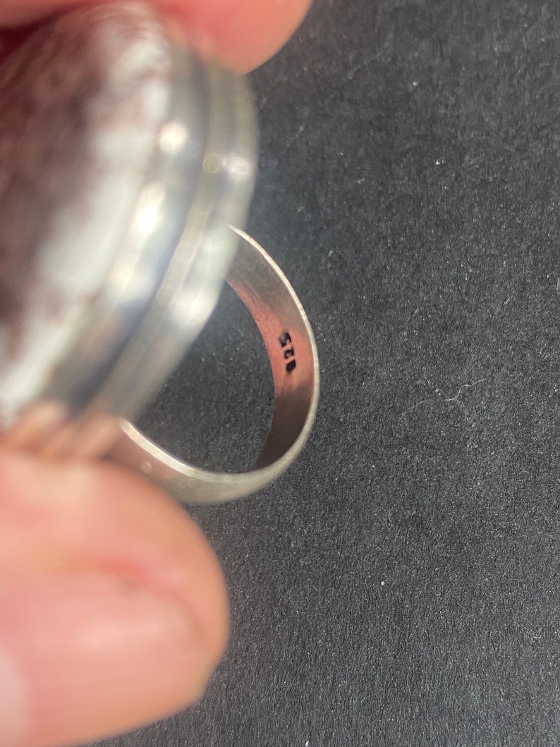 K&ouml;nnte beinhalten: Ein silberner Ring mit einer runden, glatten Oberseite und einem Band, das mit der Nummer "925" gekennzeichnet ist.