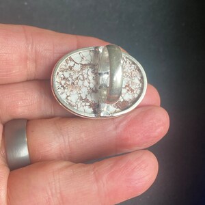K&ouml;nnte beinhalten: Ein silberner Ring mit einem wei&szlig;en und braunen Stein, der in der Mitte eingesetzt ist. Der Stein hat ein einzigartiges Muster aus wei&szlig;en und braunen Wirbeln.