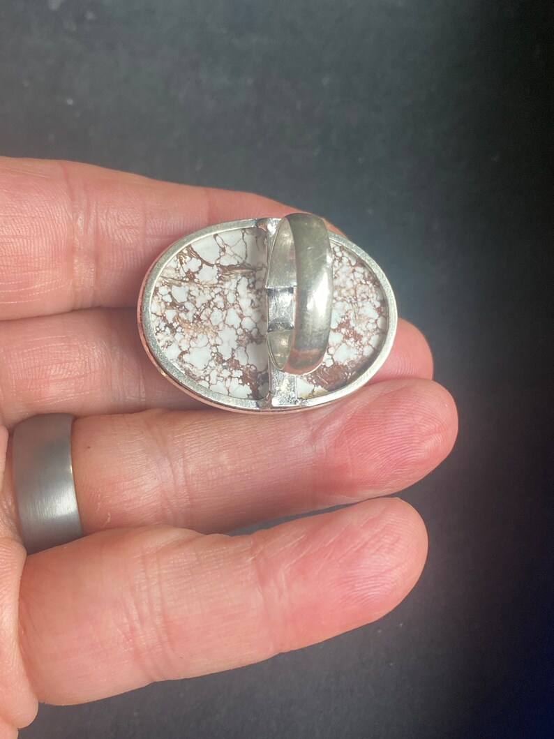 K&ouml;nnte beinhalten: Ein silberner Ring mit einem wei&szlig;en und braunen Stein, der in der Mitte eingesetzt ist. Der Stein hat ein einzigartiges Muster aus wei&szlig;en und braunen Wirbeln.