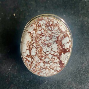 K&ouml;nnte beinhalten: Nahaufnahme eines Rings aus wei&szlig;em und braunem Achat mit einer silbernen Fassung. Der Achat hat ein wirbelndes Muster aus Wei&szlig; und Braun.