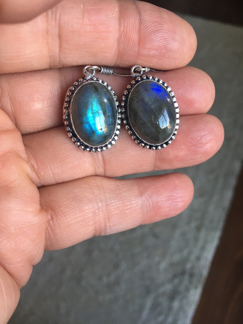 Puede incluir: Un par de pendientes de plata con piedras de labradorita de forma ovalada. Las piedras tienen una base gris oscura con destellos iridiscentes azules y verdes.