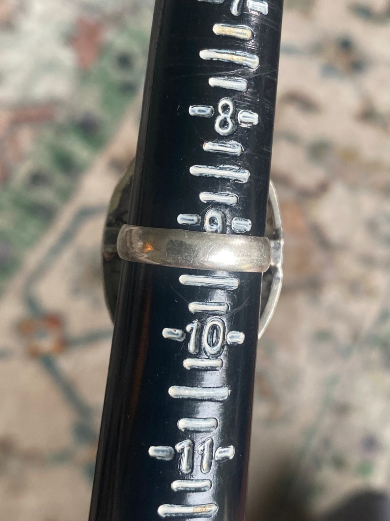 K&ouml;nnte beinhalten: Ein silberner Ring mit einem schwarzen Stein und einem silbernen Band. Der Ring ist auf einem Lineal mit der Gr&ouml;&szlig;e 10 gemessen.