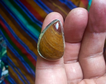 May include: A silver ring with a teardrop-shaped brown and red gemstone.