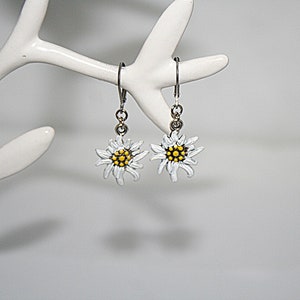 May include: A pair of silver earrings with white edelweiss flower charms. The flowers have yellow centres.