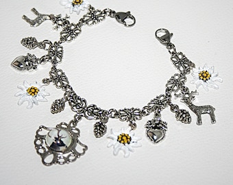 May include: Silver charm bracelet with a variety of charms, including edelweiss flowers, deer, hearts, and acorns. The bracelet is made of a silver chain with a lobster clasp.