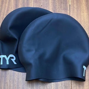 May include: Two black silicone swim caps with the TYR logo in white.