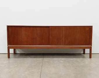 May include: A long, rectangular wooden sideboard featuring a warm brown finish with a visible wood grain. The piece is supported by four straight legs and includes two sliding doors that span the length of the front, creating a clean, flat surface.