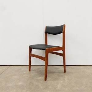May include: A mid-century modern chair with a black seat and backrest. The chair has a wooden frame with a natural finish. The design features a simple, elegant silhouette, suitable for dining or as an accent piece. The chair's dimensions are approximately 30 inches high.