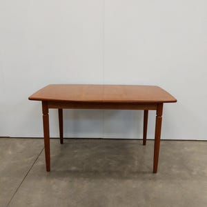 May include: A light brown wooden dining table with four legs. The table has a rectangular top with rounded corners. The legs are slender and slightly tapered. The table is approximately 60 inches long.