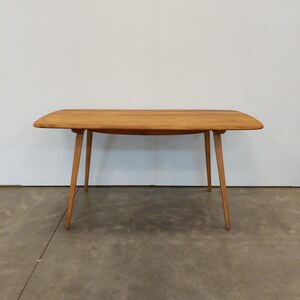 May include: A light brown wooden table with a rectangular top and four angled legs. The table is approximately 60 inches long and 30 inches wide. The legs are thin and tapered, and the table has a mid-century modern design.