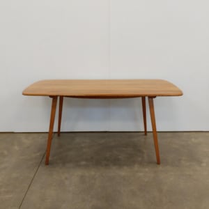 May include: A white ceramic mug with a black handle and the text "But First, Coffee" in a bold, black font. The mug is set against a blurred background, suggesting a cozy setting.