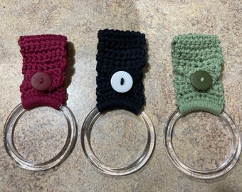 May include: Three crocheted towel rings with buttons. The rings are made in burgundy, black, and green.