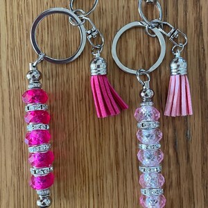 May include: Two pink and clear crystal beaded keychains with silver key rings and pink tassels.