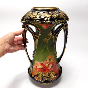 Op de afbeelding: Een vaas in Art Nouveau-stijl met een donkerblauw, goud en groen kleurenschema. De vaas heeft een bloemenontwerp met rode en oranje klaprozen. De vaas is ongeveer 30 cm hoog.
