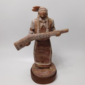 May include: A hand-carved alabaster sculpture of a Native American man holding a long, decorated pipe. The sculpture is painted in shades of brown, white, and red.