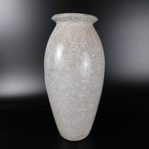 Może przedstawiać: Biały ceramiczny wazon z pękniętą glazurą. Wazon ma zaokrąglone ciało i wąski otwór.