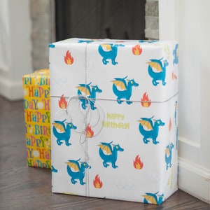 May include: Two wrapped gifts, one with a yellow and pink pattern that says "Happy Birthday" and the other with a white background and blue dragons with the text "Happy Birthday!"