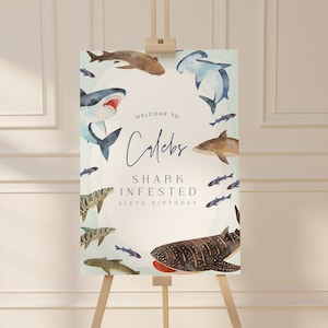 May include: Welcome to Cole's Shark Infested Sixth Birthday party sign with a blue and white watercolor design featuring various sharks, fish, and a whale shark.