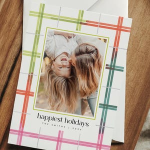 May include: Holiday greeting card with a family photo inside a green border. The card has a plaid pattern in pink, green, and orange. The text "happiest holidays" is printed on the card, along with the family name and year.