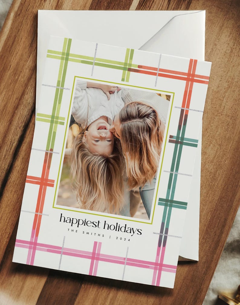 May include: Holiday greeting card with a family photo inside a green border. The card has a plaid pattern in pink, green, and orange. The text "happiest holidays" is printed on the card, along with the family name and year.