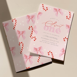 May include: Pink and white invitation with a candy cane and bow pattern. The text reads "Sweet One" and includes details for Aubrey's first birthday party.