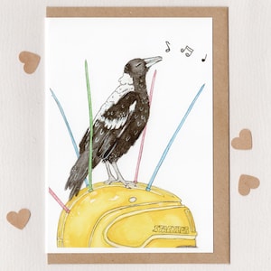 May include: Greeting card featuring a watercolor illustration of a black and white bird singing. The bird is perched on a yellow helmet with the word "STACKHAT" printed on it. Colorful lines radiate from the helmet. The card is framed in brown.