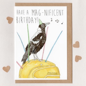 May include: A birthday card with a watercolor illustration of a magpie wearing a party hat and singing. The card reads "Have a Mag-nificent Birthday!" and features musical notes and colorful candles.