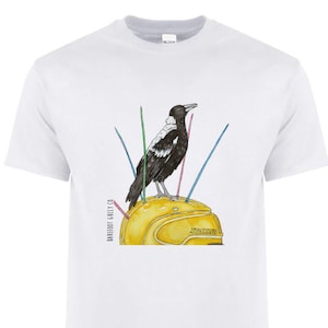 May include: White t-shirt with a watercolour illustration of a black and white bird on a yellow helmet. The helmet has colourful lines radiating from it. The text "Barefoot Gully Co" is printed on the left side.