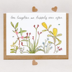 May include: A greeting card with a watercolor illustration of various wildflowers in shades of yellow, red, pink, and blue. The card reads "love laughter and happily ever after" in black script. Three small, brown heart-shaped cutouts are scattered around the card.