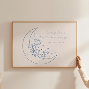 May include: A framed print featuring a blue crescent moon, flowers, and stars. The text "long live all the magic we made" is written in a delicate script. The frame is made of light-colored wood.