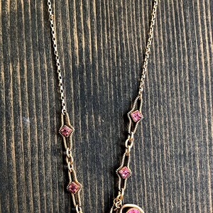 May include: A gold-toned necklace with pink gemstones. The necklace features a delicate chain with alternating pink square and oval-shaped stones. The gemstones are set in gold-colored metal, creating a vintage aesthetic.