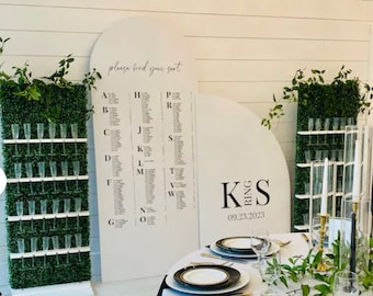 May include: A white round table with a white tablecloth and black napkins. There are gold rimmed white plates, gold silverware, and clear glasses on the table. There are black and gold candlesticks and greenery on the table. A white sign with the text "KS Ring 09.23.2023" is in the background.