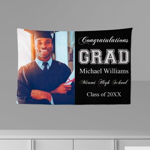 May include: Black and white graduation banner with a photo of a graduate wearing a cap and gown. The banner says "Congratulations Grad" with the graduate's name, school, and class year.