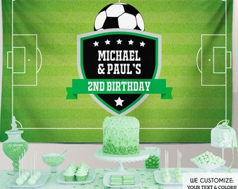 May include: A green soccer-themed birthday party backdrop with a soccer ball and a shield that reads "MICHAEL & PAUL'S 2ND BIRTHDAY." The backdrop is 6 feet by 4 feet. A table is set with a cake, cupcakes, and other treats.