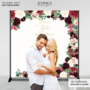 May include: A white backdrop with a floral design in shades of burgundy, pink, and green. The backdrop is decorated with a couple's names, "Mr. & Mrs. Yoli", and the text "CHR CANDACE". The backdrop is 8 feet by 8 feet and is suitable for any type of event.
