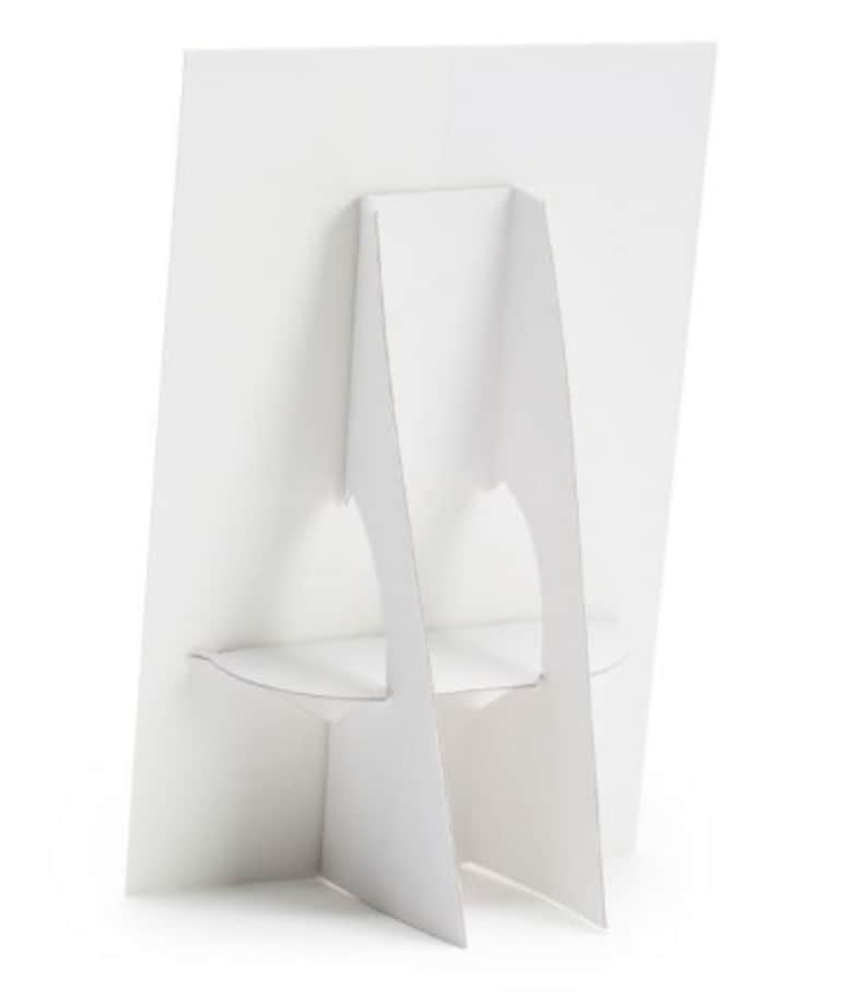 May include: White cardboard display stand with a rectangular base and two vertical supports. The stand is designed to hold a sign or poster.