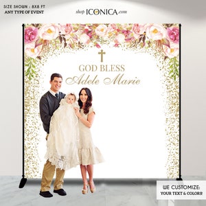 May include: A white backdrop with a gold glitter and floral design. The text "GOD BLESS Adele Marie" is written in gold script. A family of three is standing in front of the backdrop.
