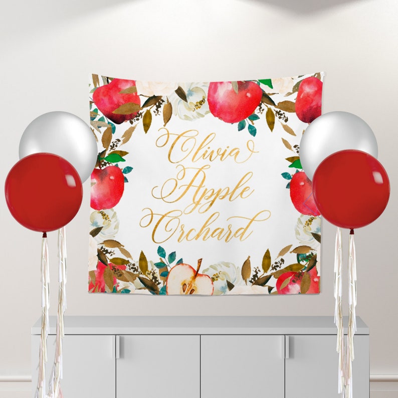 May include: A white backdrop with a watercolor design of red apples, green leaves, and white flowers. The text "Olivia's Apple Orchard" is written in gold script.