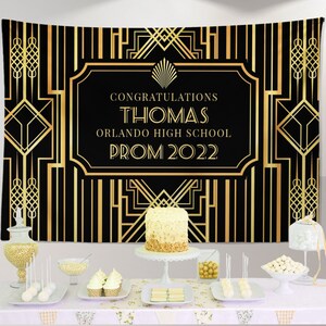 May include: A black and gold art deco themed backdrop with the text "Congratulations Thomas Orlando High School Prom 2022". The backdrop is decorated with geometric patterns and a fan-shaped design.