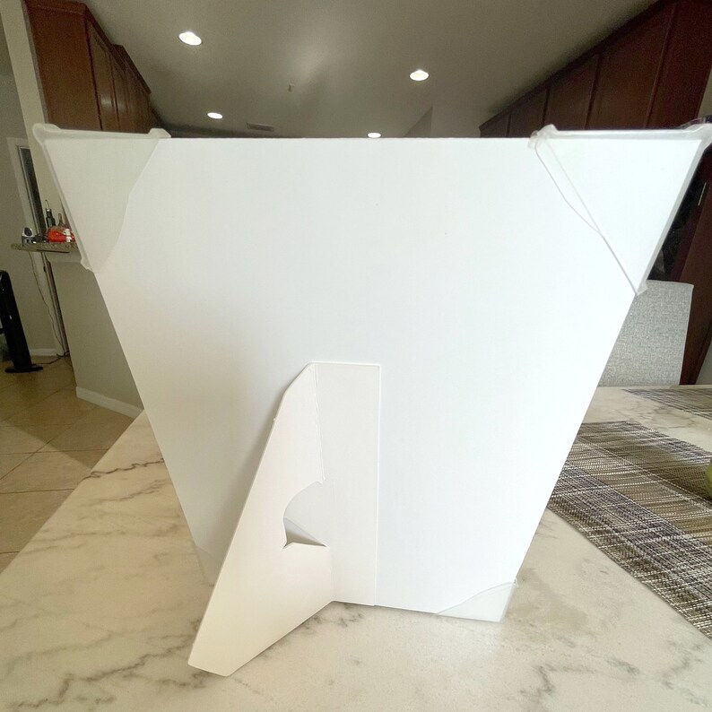 May include: White cardboard easel stand with a white rectangular sign. The stand has a triangular base and a slot for the sign to be inserted.