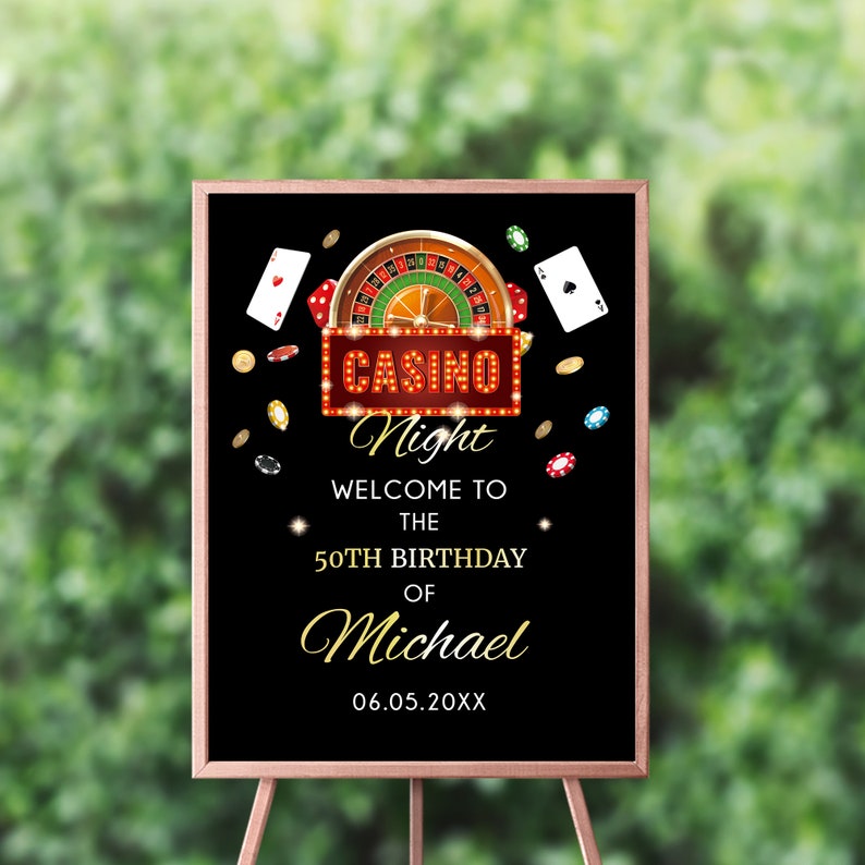 May include: A black sign with a gold frame on a wooden easel. The sign reads "Casino Night" with a roulette wheel and playing cards graphic. The text welcomes guests to the 50th birthday of Michael, with the date below.