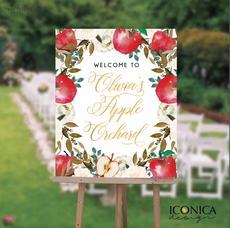 May include: Welcome to Olivia's Apple Orchard sign with a white background and a wreath of red apples, white flowers, and green leaves. The text is in gold script.