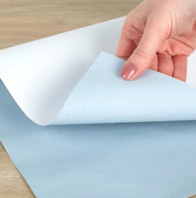 Op de afbeelding: Een vel wit papier met een lichtblauw vel papier eronder. Het bovenste vel wordt opgetild om het onderste vel te laten zien.